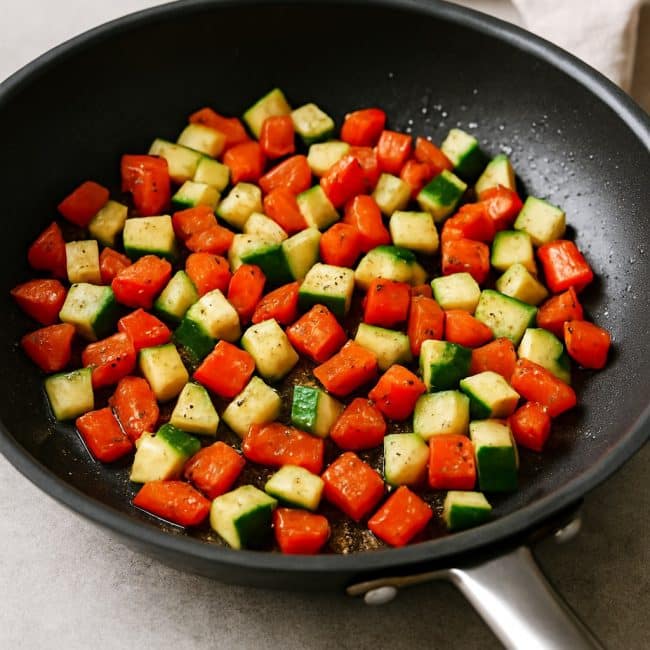 Paprika und Zucchini werden in der Pfanne für die Couscous-Bowl angebraten