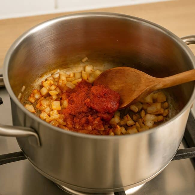 Zwiebeln und Knoblauch werden in einem Edelstahl-Topf mit Öl und Tomatenmark auf dem Herd angebraten – Vorbereitung für eine herzhafte Linsensuppe.