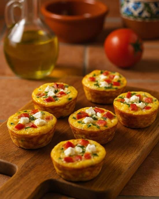 Fünf spanische Ei-Muffins mit Paprika und Feta auf einem Holzbrett, angerichtet in einer hellen Küche mit spanischem Flair.