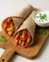 Zwei Chicken Fajita Wraps mit Hähnchen, Paprika und Kräuterdip auf Holzbrett serviert