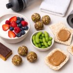 Eine Auswahl proteinreicher Fitness-Snacks wie Quark mit Beeren, Energy Balls und Edamame auf einem Tisch