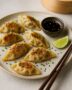 Frisch gebratene Gyoza mit Sojadip auf Keramikteller angerichtet, daneben Stäbchen und Limette