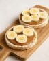 Zwei belegte Reiswaffeln mit Mandelmus und Bananenscheiben auf Holzbrett