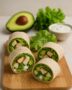 Geschnittene Wraps mit Hähnchen, Avocado und Salat auf Holzbrett